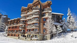 Ein mehrstöckiges Holzgebäude mit Balkonen, umgeben von schneebedeckten Bäumen und einem strahlend blauen Himmel.