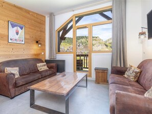 A cozy living room with two brown leather sofas, a wooden coffee table, and a large window offering a view of a mountainous landscape.