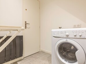 A laundry room with a washing machine, a door with a handle, and a staircase with a handrail.