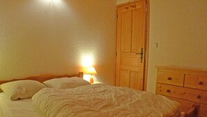 A bedroom with a bed, a nightstand with a lamp, a wooden wardrobe, and a dresser. - Cozy apartment in Morillon, 6 people, near Criou (Morillon Village)