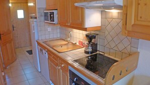 A compact kitchen with wooden cabinets, a microwave, a coffee maker, and a stove. - Cozy apartment in Morillon, 6 people, near Criou (Morillon Village)