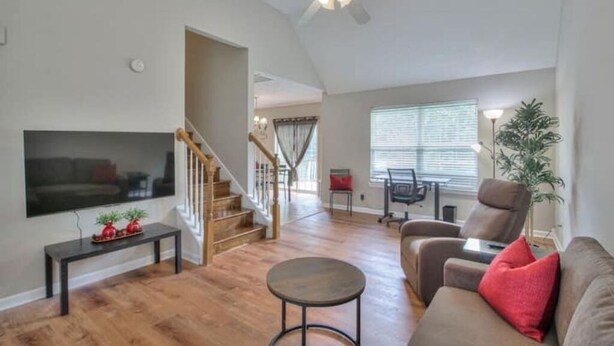 A modern living room with hardwood flooring, a flat-screen TV, a round coffee table, and a brown sofa with red cushions. - Modern 3/2.5 near everything! Smryna- Off I-24! (Smyrna)