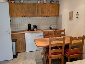 Eine kompakte Küche mit Holzschränken, einem weißen Geschirrspüler und einem Esstisch mit Stühlen.