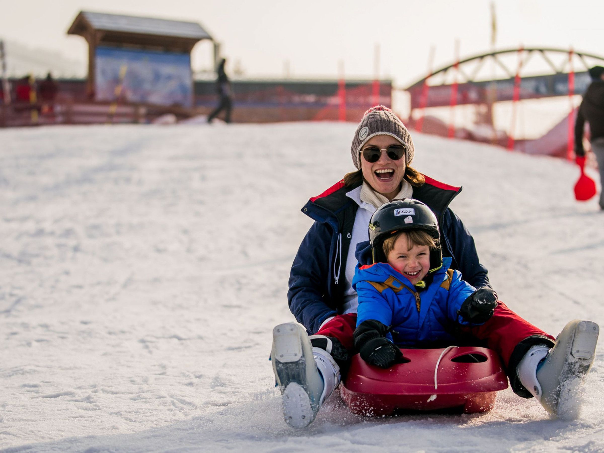 Une personne portant une veste bleue et un pantalon rouge dévale une pente enneigée en luge.