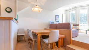 A cozy living area with a wooden table, four chairs, a sofa, and a staircase.