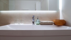 A bathroom with a white sink, two clear glasses, a soap dispenser, a towel, and a woven basket.