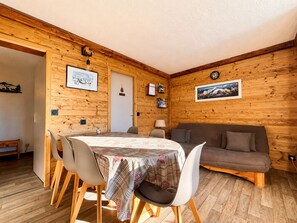 Ein gemütliches Zimmer mit Holzeinrichtung, einem Esstisch mit Stühlen, einer Couch und einer Uhr an der Wand.