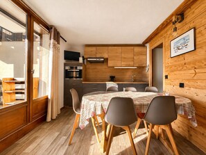 Eine kleine Küche mit Holzausbau, einem Esstisch mit Stühlen und einem Fernseher über der Arbeitsfläche.