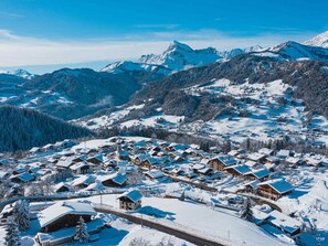 Ein verschneites Dorf mit traditionellen Holzhäusern, einer Kirche und Bergen im Hintergrund.