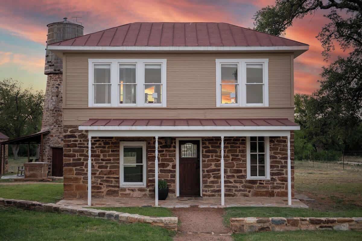 A two-story house with a stone foundation and a metal roof.