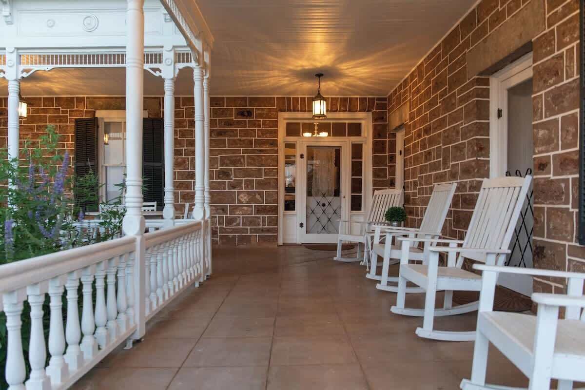 A covered porch with white railings, a brick wall, and white rocking chairs.