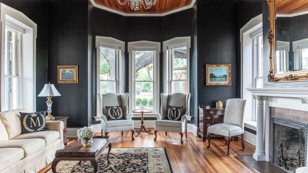 Una sala de estar formal con chimenea, sillones elegantes y un espejo grande.