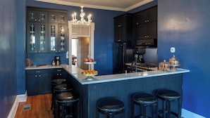 A modern kitchen with dark blue cabinetry, a central island with stools, and a chandelier. - The Mildred Haus (Mason)