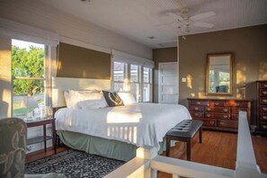 A bedroom with a large bed, a dresser, a bench, and a window with a view of greenery. - The Mildred Guest Haus (Mason)