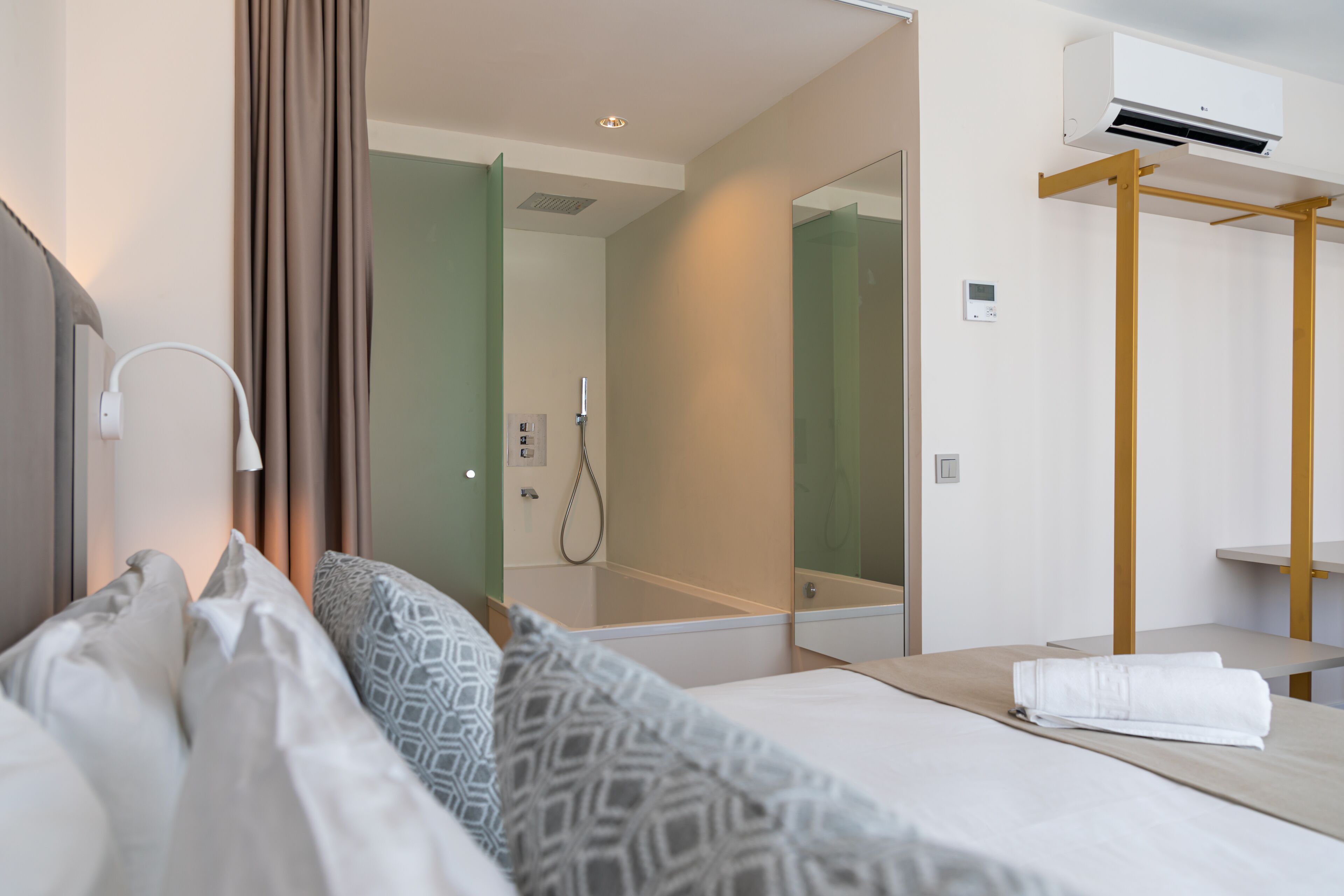 Une chambre d’hôtel comprenant un lit, une table de chevet avec une serviette, un miroir, un appareil de climatisation et un espace douche.