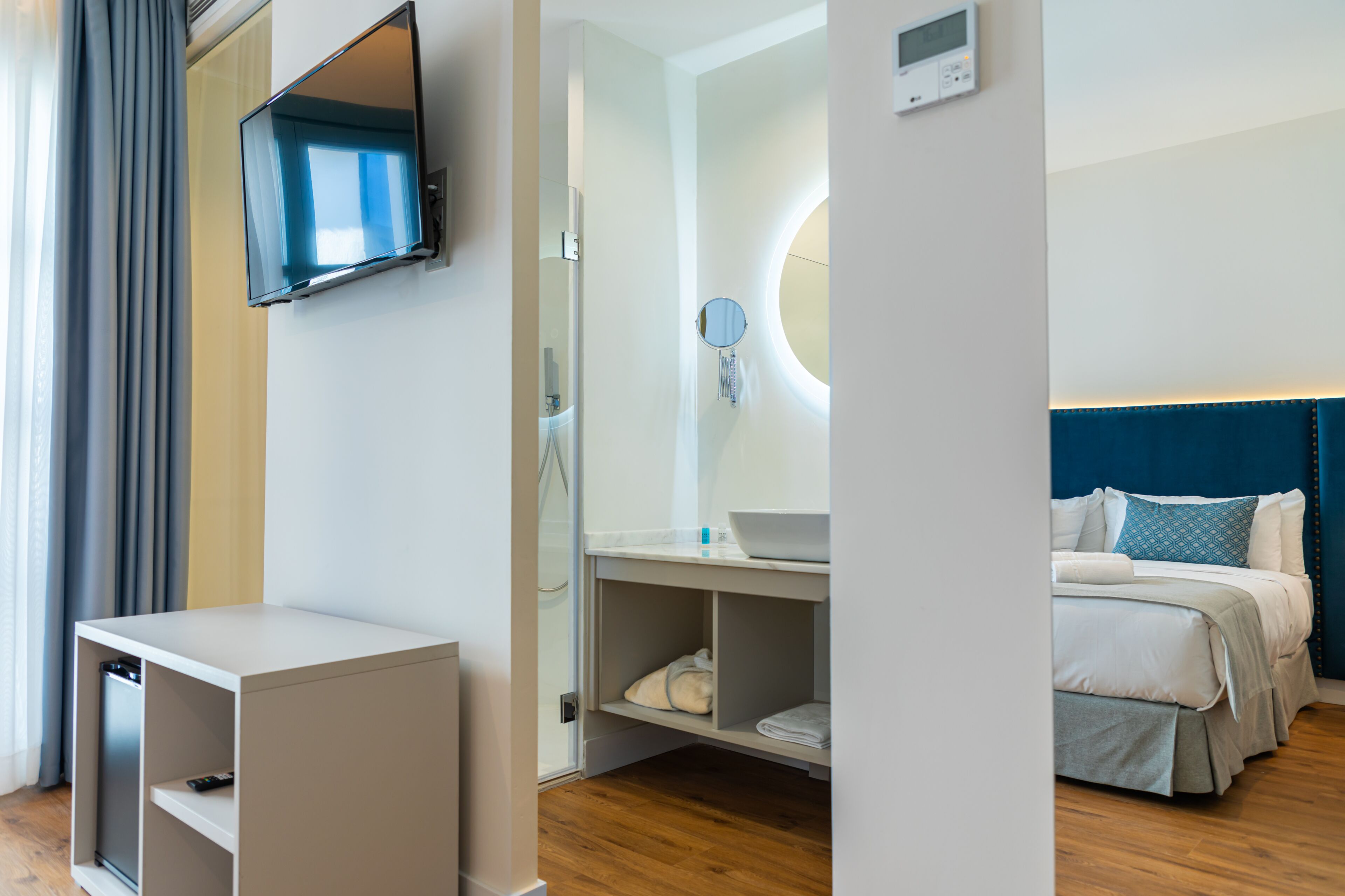 Habitación de hotel con cama, mesita de noche, televisor y baño con espejo y lavamanos.