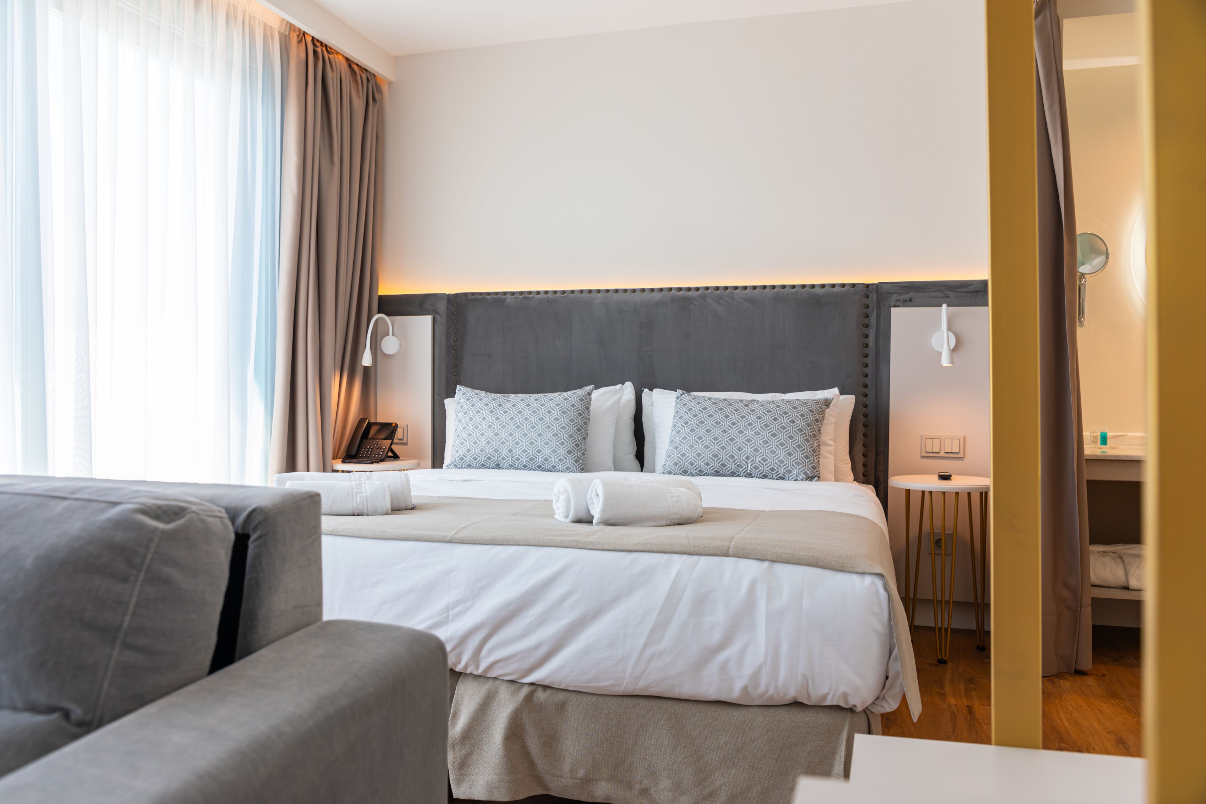 A modern hotel room with a large bed, a bedside table, a lamp, and a view of the outside.