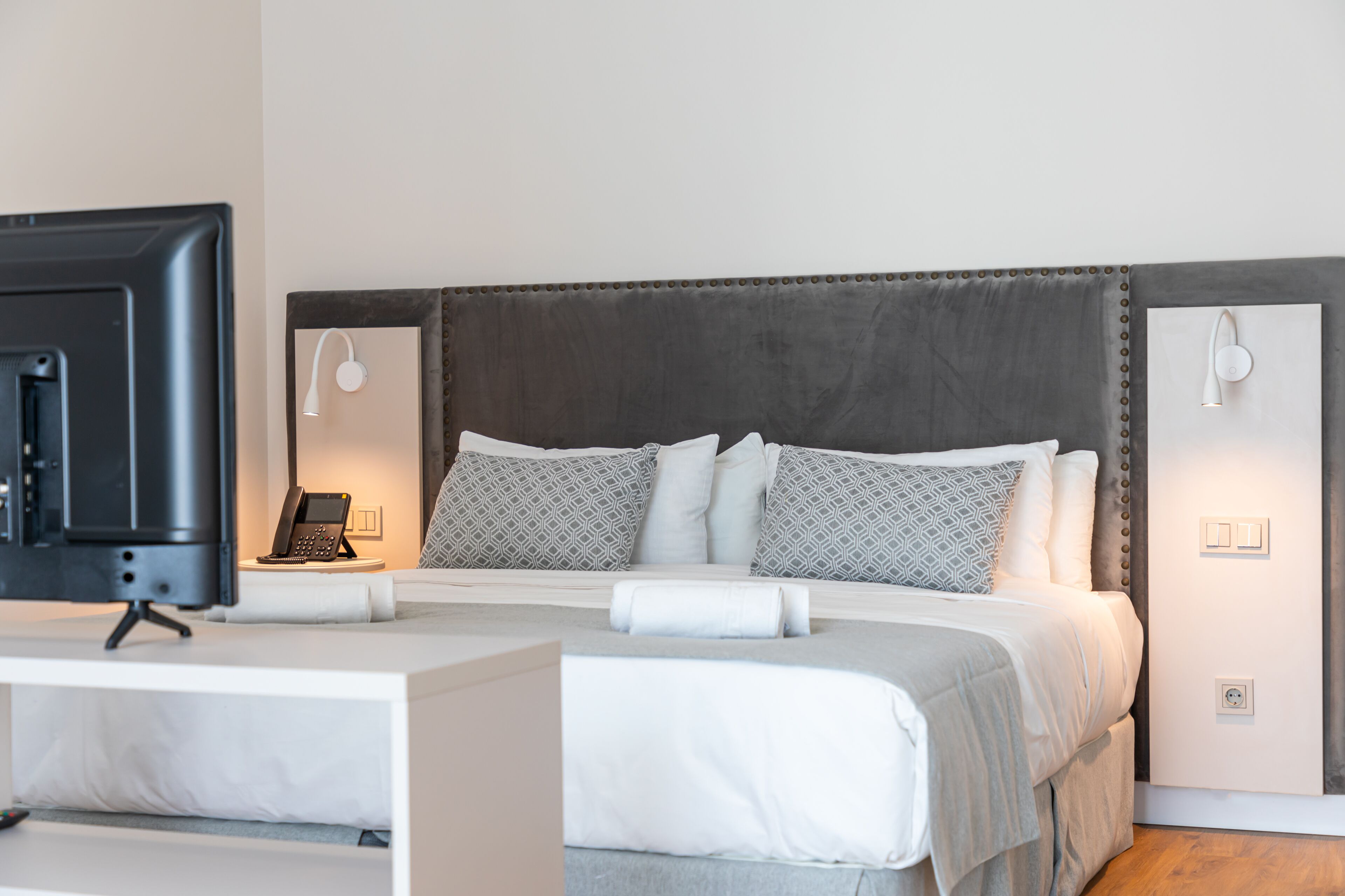 A neatly arranged hotel room with a large bed, bedside lamps, a desk with a television, and a telephone.