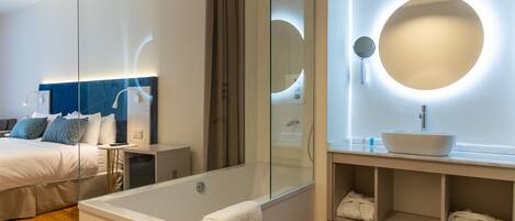 A modern bedroom with a large bed, a glass-enclosed shower, and a vanity with a round mirror.