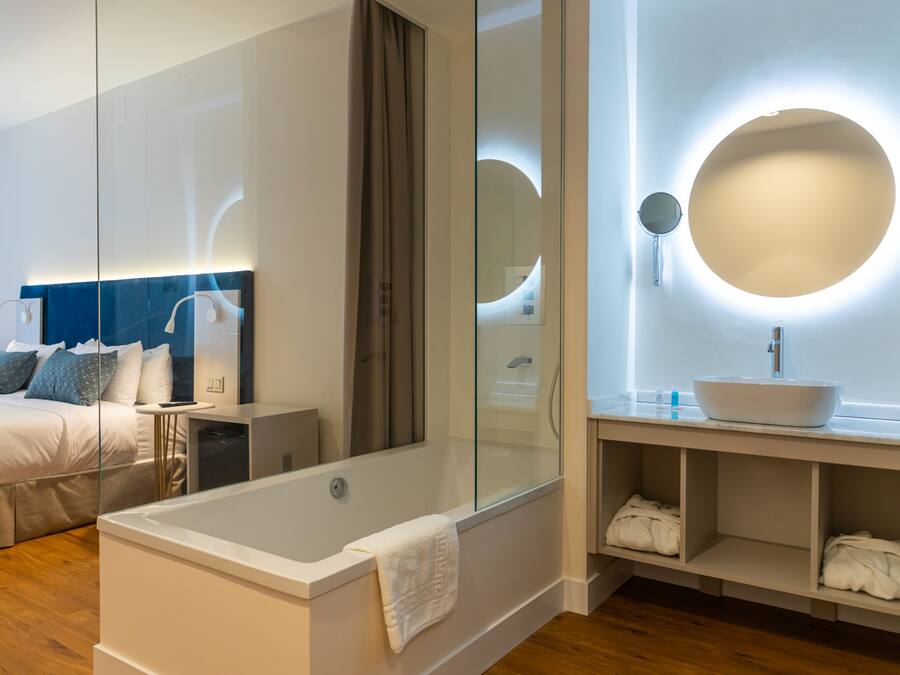 Un dormitorio moderno con una cama grande, cabina de ducha con paredes de vidrio y tocador con espejo redondo.