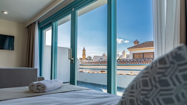Una habitación de hotel con cama, televisión montada en la pared y un amplio ventanal con vistas a la ciudad.