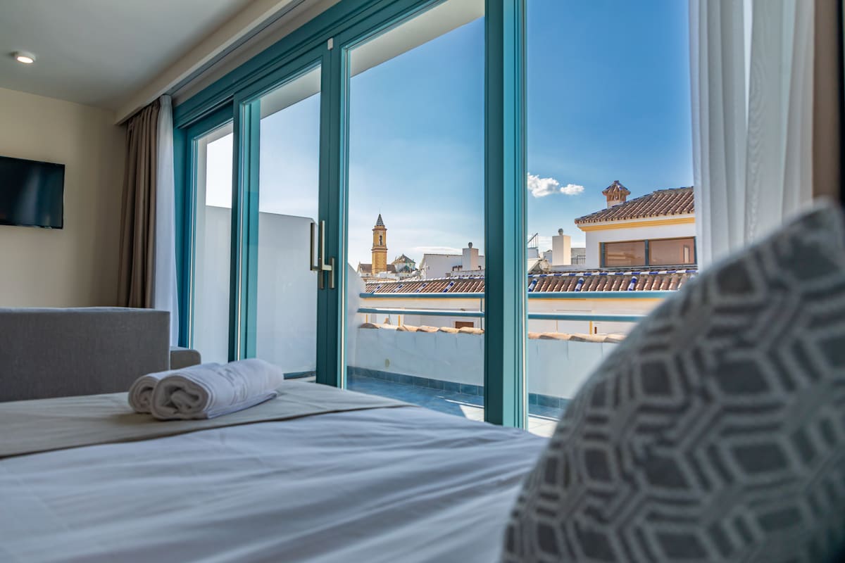 Una habitación de hotel con cama, televisión montada en la pared y un amplio ventanal con vistas a la ciudad.