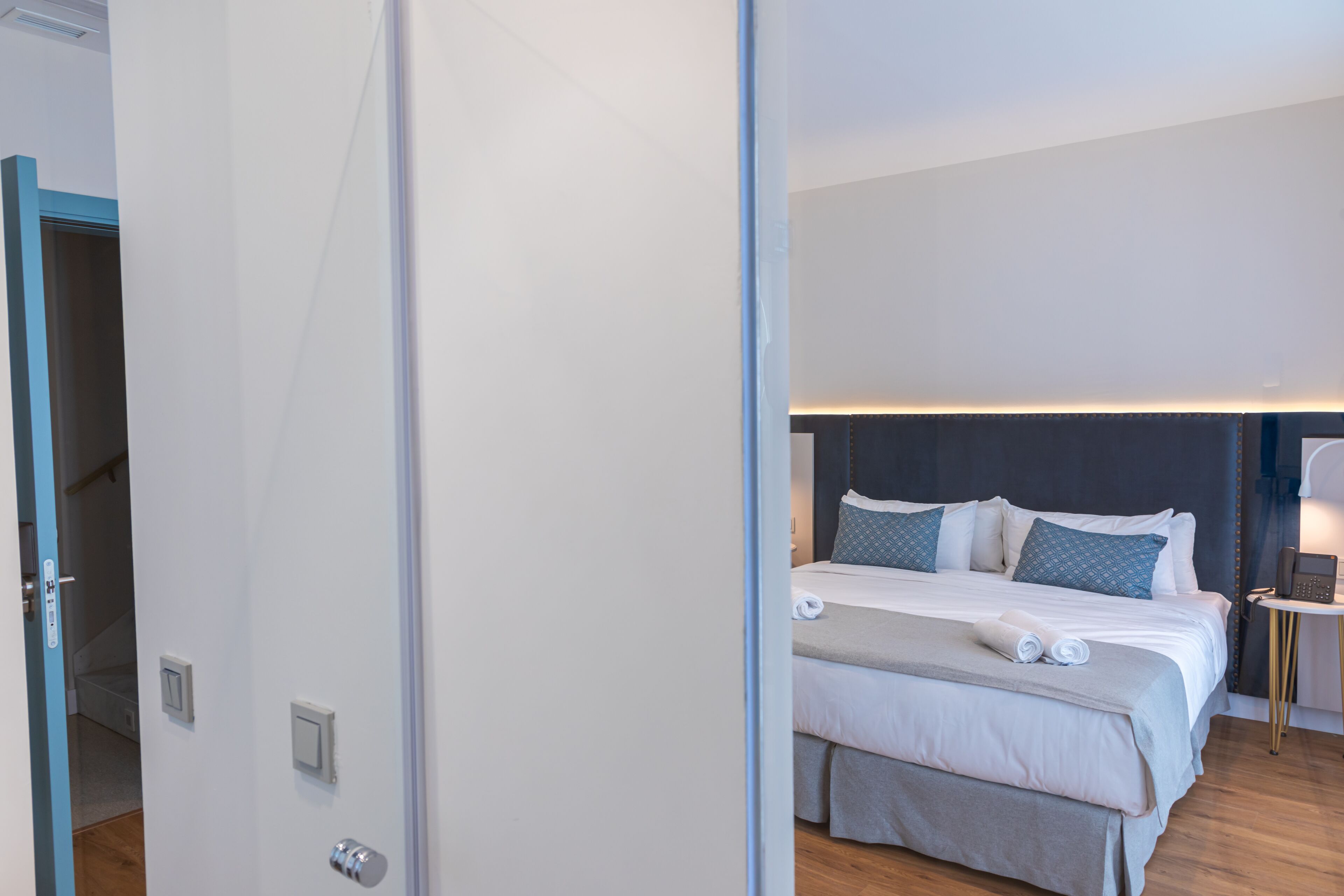 Ein modernes Hotelzimmer mit einem ordentlich bezogenen Bett, einem Nachttisch mit einer Lampe und einem an der Wand befestigten Telefon.