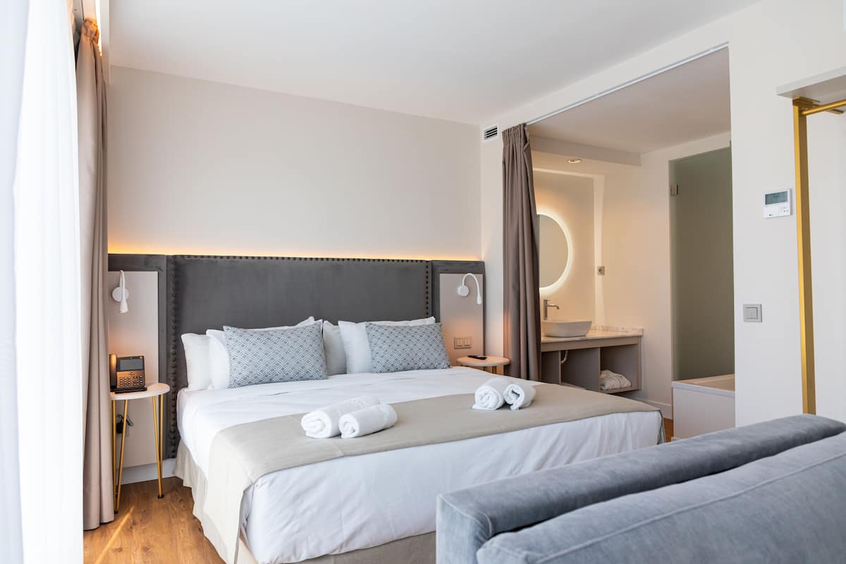 Una habitación de hotel moderna con una cama grande, mesitas de noche, baño y zona de estar.