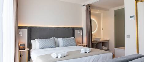 A modern hotel room with a large bed, bedside tables, a bathroom, and a seating area.