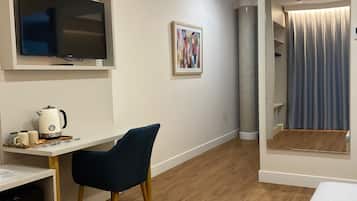 Una habitación moderna con una televisión de pantalla plana montada en la pared, un escritorio con una silla, una cafetera y un mueble pequeño.