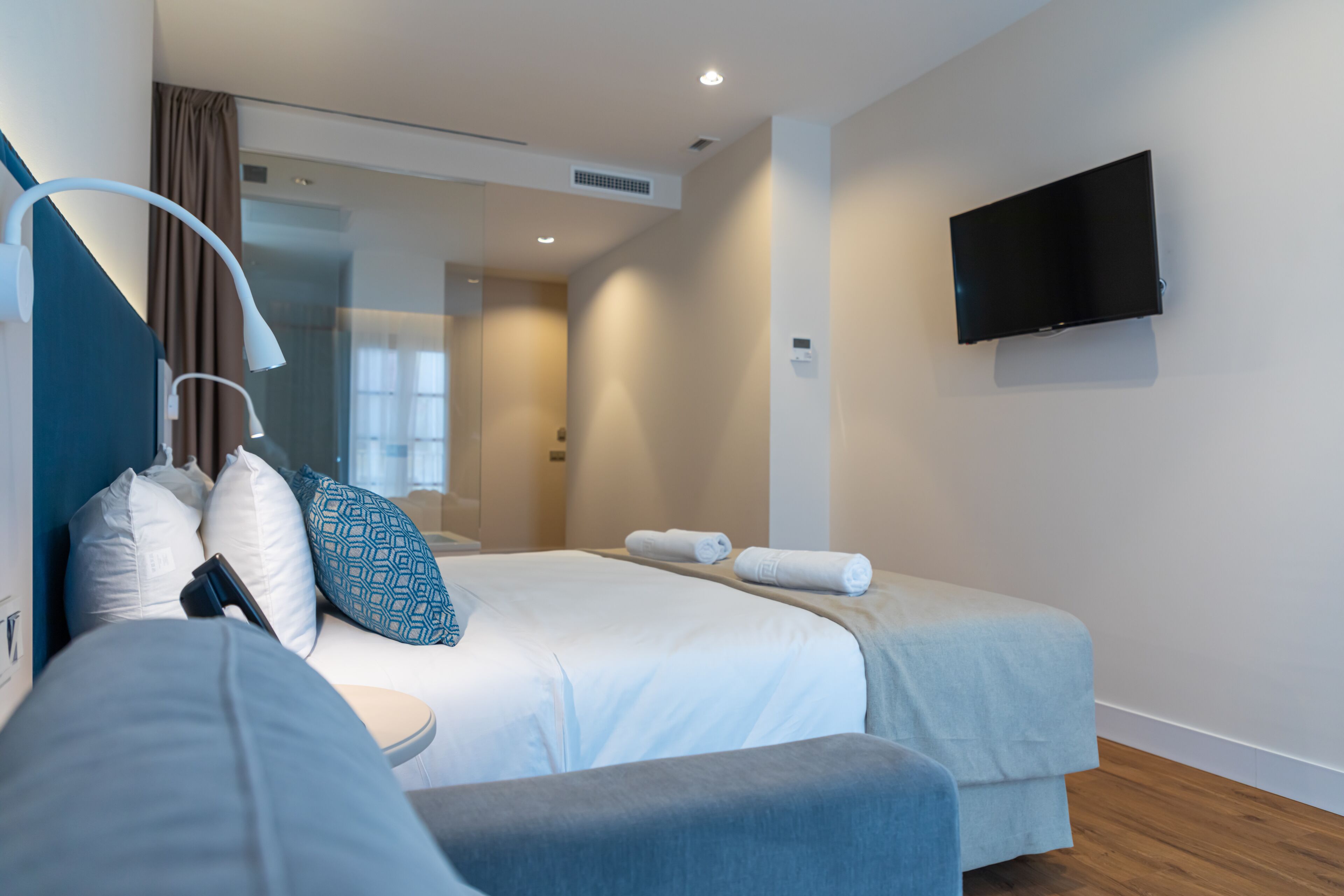 Una habitación de hotel moderna con una cama, un televisor montado en la pared y una ventana con cortinas.