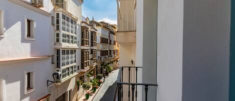 Una calle estrecha flanqueada por edificios, con balcones que tienen barandillas y macetas.
