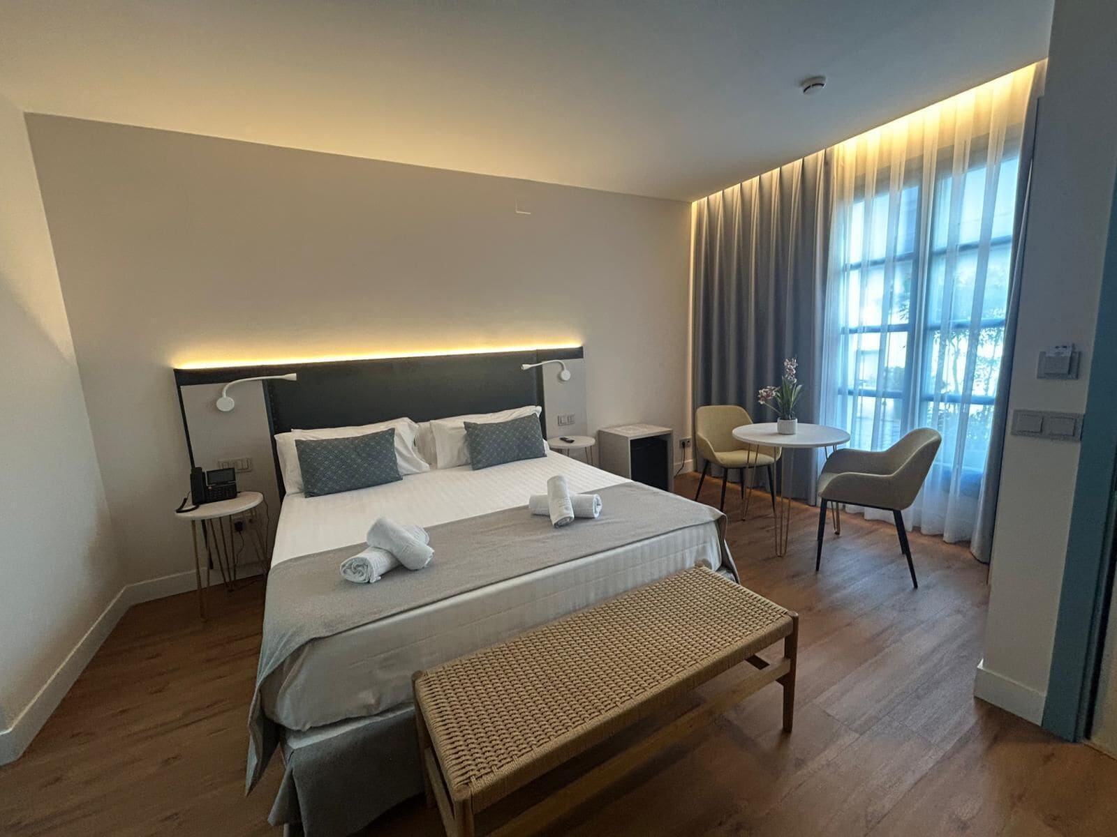 Ein modernes Hotelzimmer mit einem großen Bett, Nachttischen, einem Schreibtisch, einem Sessel und einer Bank.