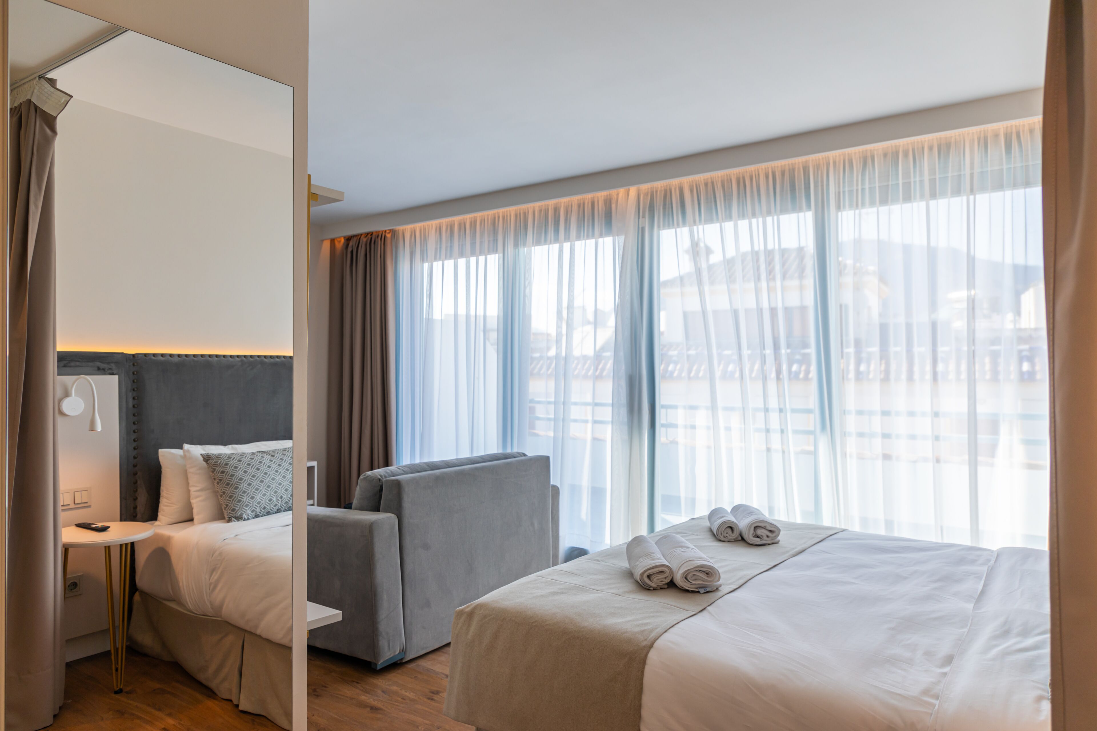 Habitación de hotel con cama, una silla, un escritorio y un ventanal con cortinas.