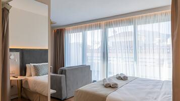 Habitación de hotel con cama, una silla, un escritorio y un ventanal con cortinas.