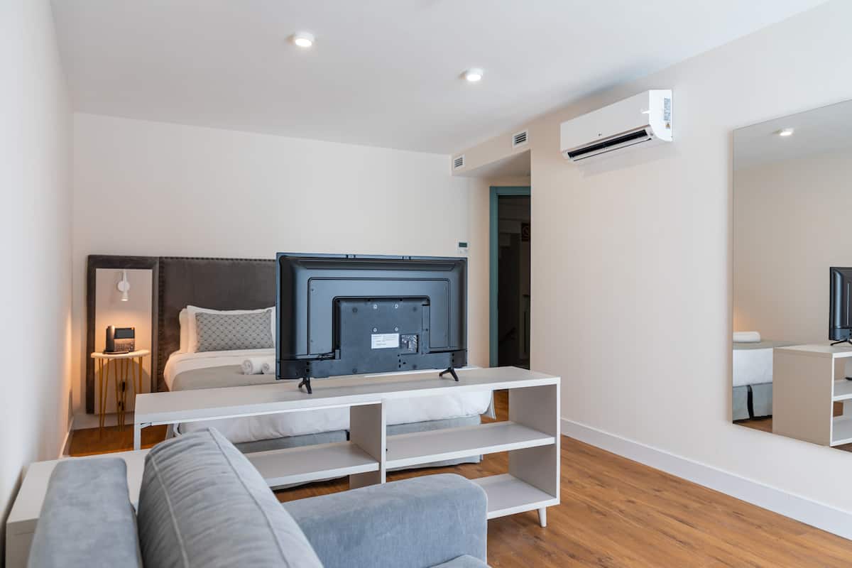 Una habitación de hotel moderna con una cama, un televisor en un mueble bajo, un sofá y un espejo grande.