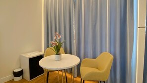 Una habitación moderna con una mesa redonda, dos sillas, una planta pequeña y una cortina con iluminación integrada.