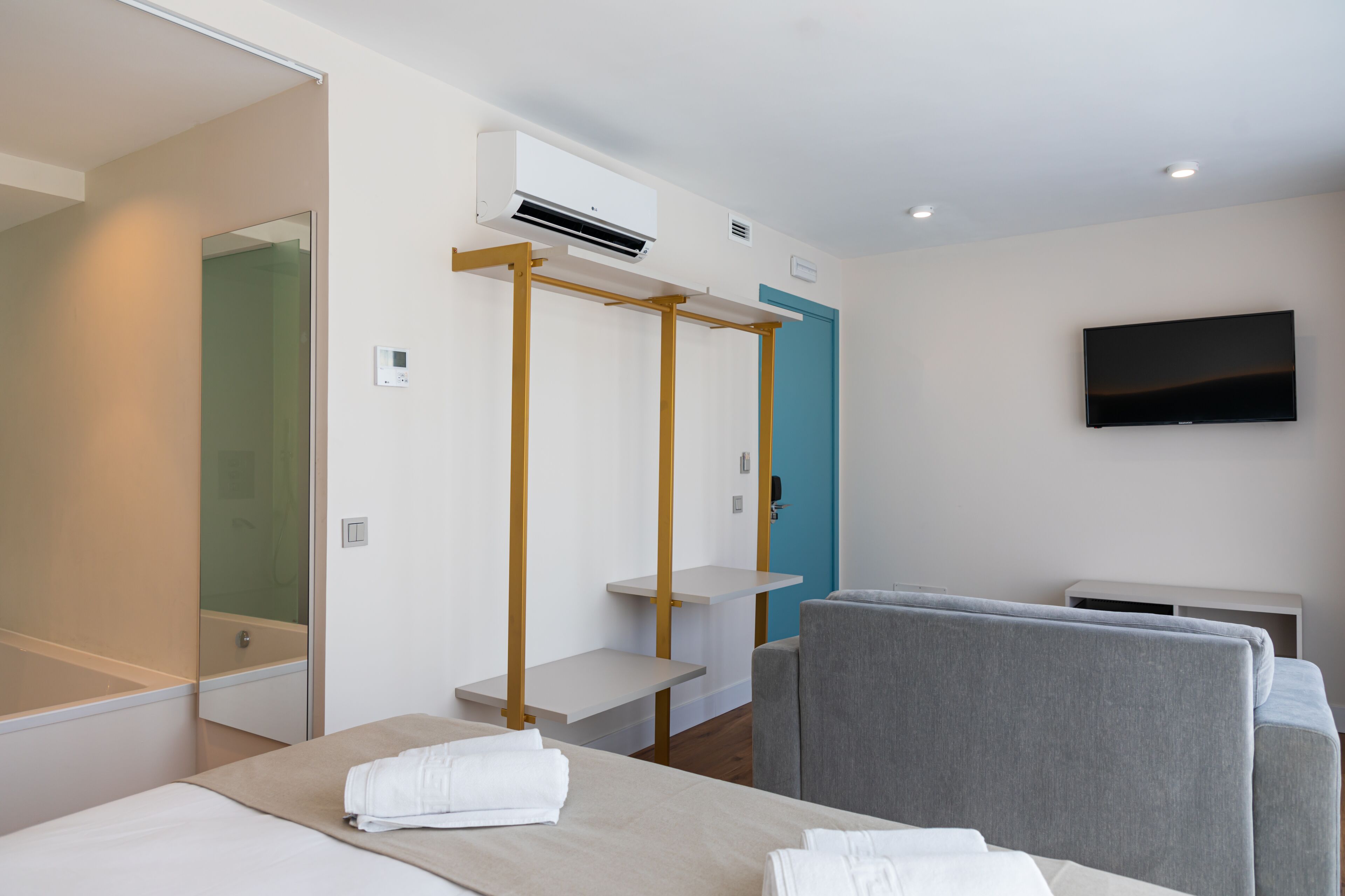 A hotel room with a bed, a TV, a shower, and a blue door.