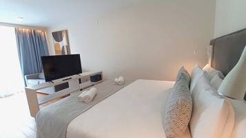 Habitación de hotel moderna con una cama grande, un televisor de pantalla plana, una mesita de noche con lámpara y vistas al exterior.