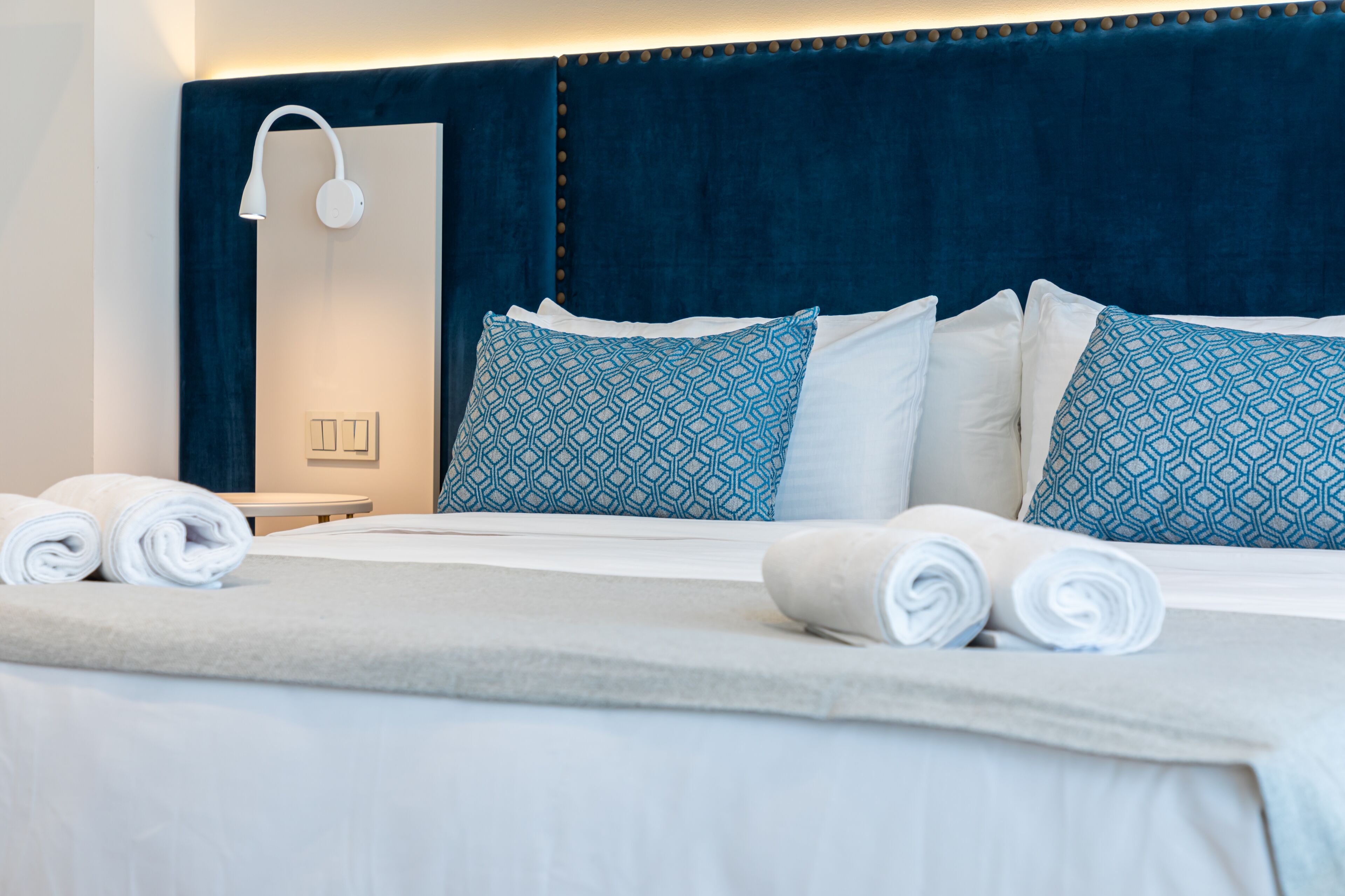 A neatly made bed with blue patterned pillows, a white headboard, and a wall-mounted light fixture.