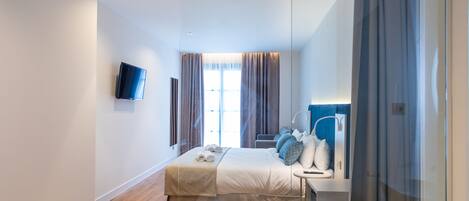 A modern hotel room with a large bed, a bedside table with a lamp, a TV, and a bathroom with a bathtub.