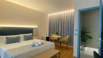 Una habitación de hotel moderna con una cama grande, mesitas de noche, una pequeña mesa redonda con sillas, un banco y una planta en maceta.