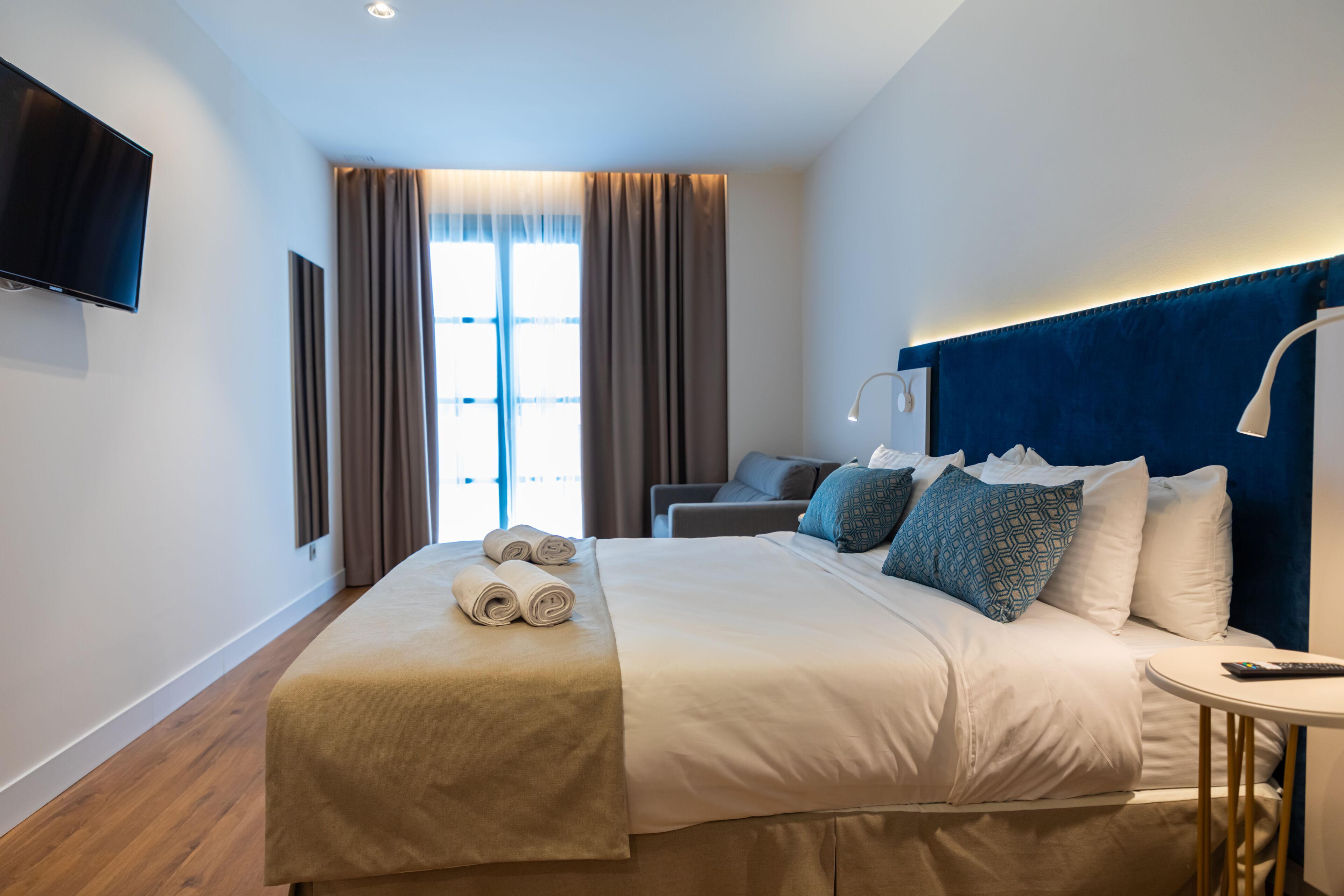 Een hotelkamer met een groot bed, een flatscreen televisie aan de muur, een bureau met een lamp en uitzicht op het landschap.