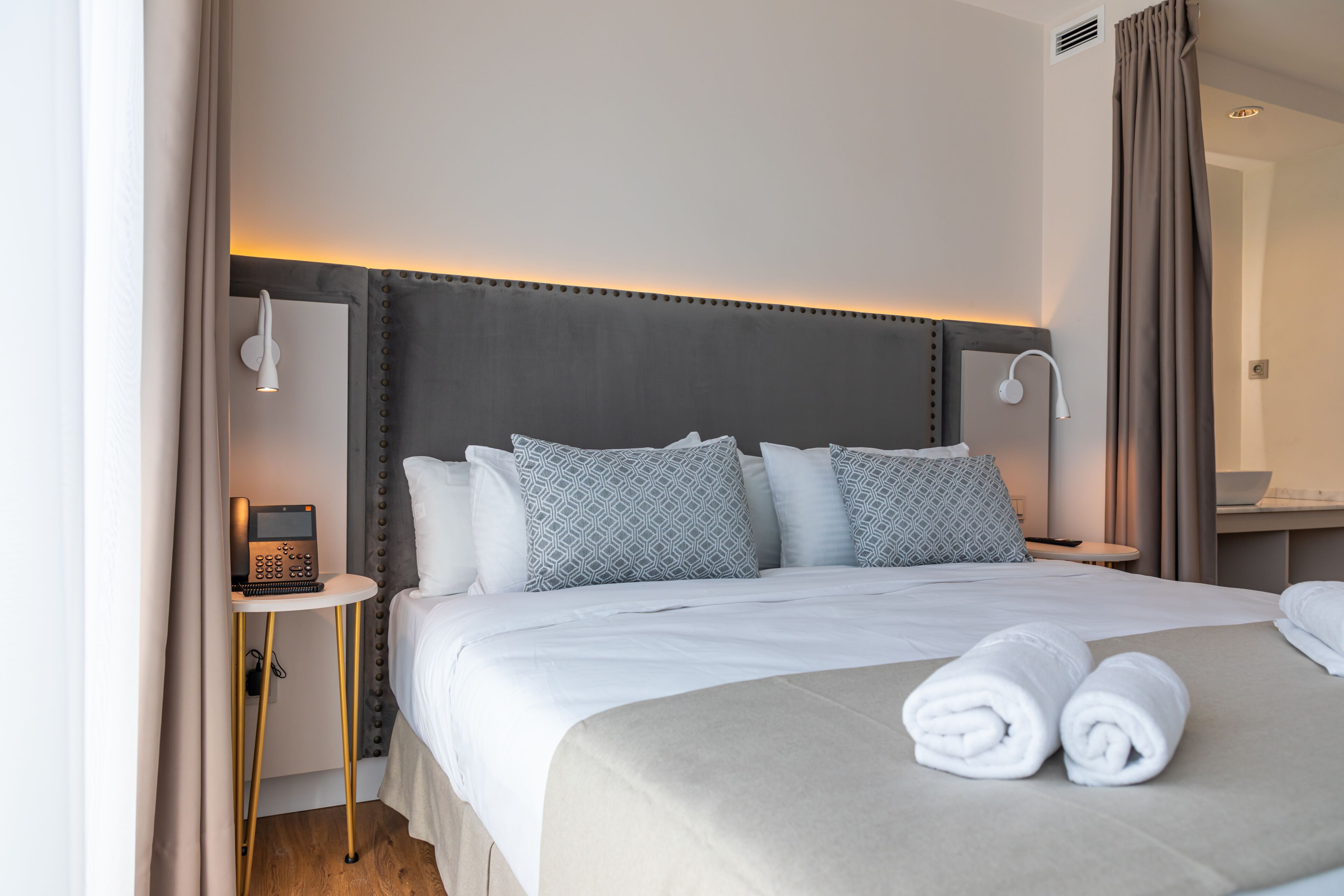 Habitación de hotel con una cama grande, dos mesitas de noche, un tocador, un espejo y zona de baño.