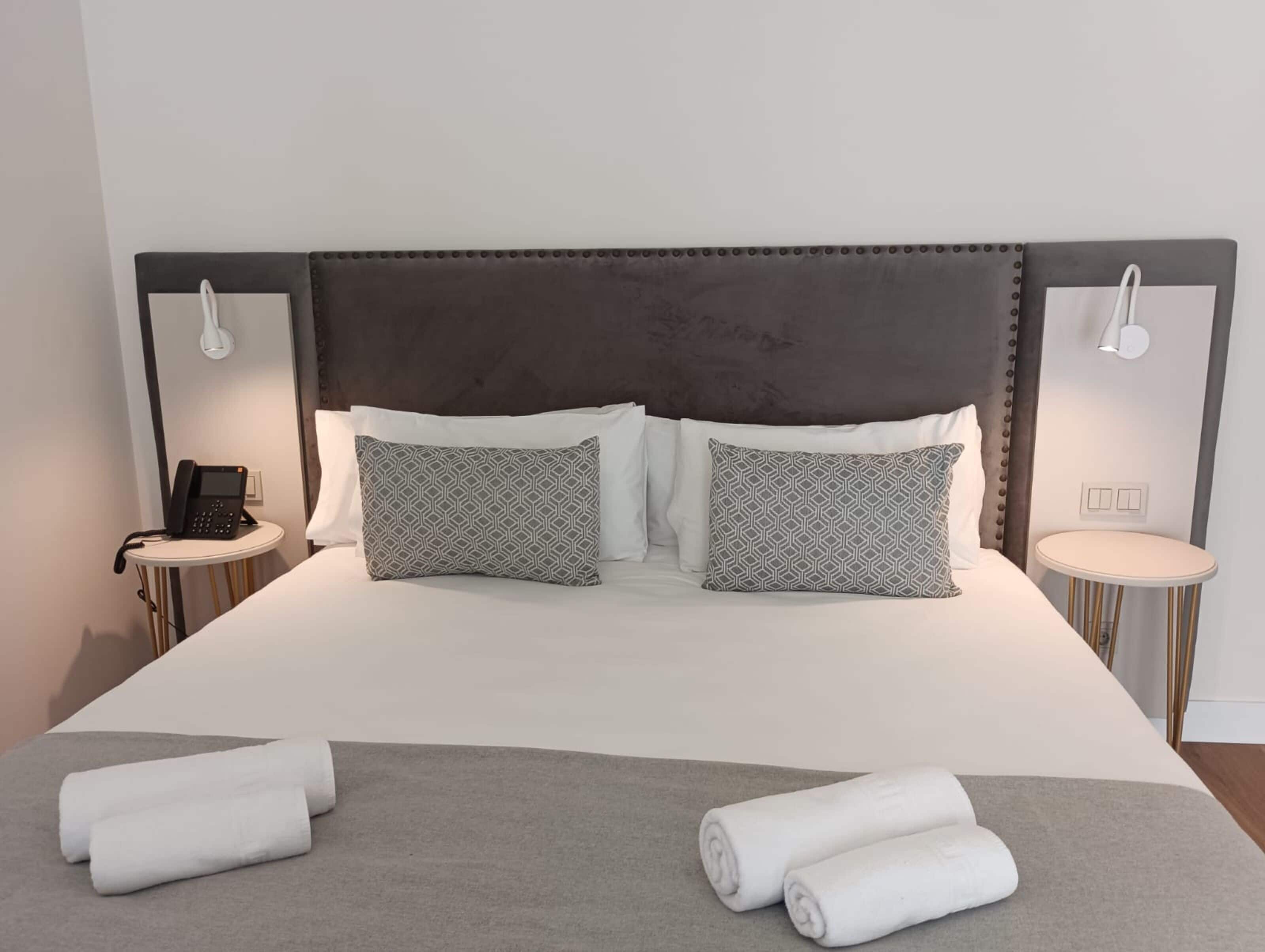 Ein Hotelzimmer mit einem großen Bett, zwei Nachttischen, einem Telefon und zwei Lampen.