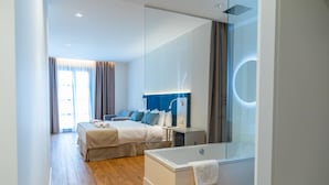 Una habitación de hotel moderna con una cama grande, una bañera con mampara de vidrio y un espejo amplio.