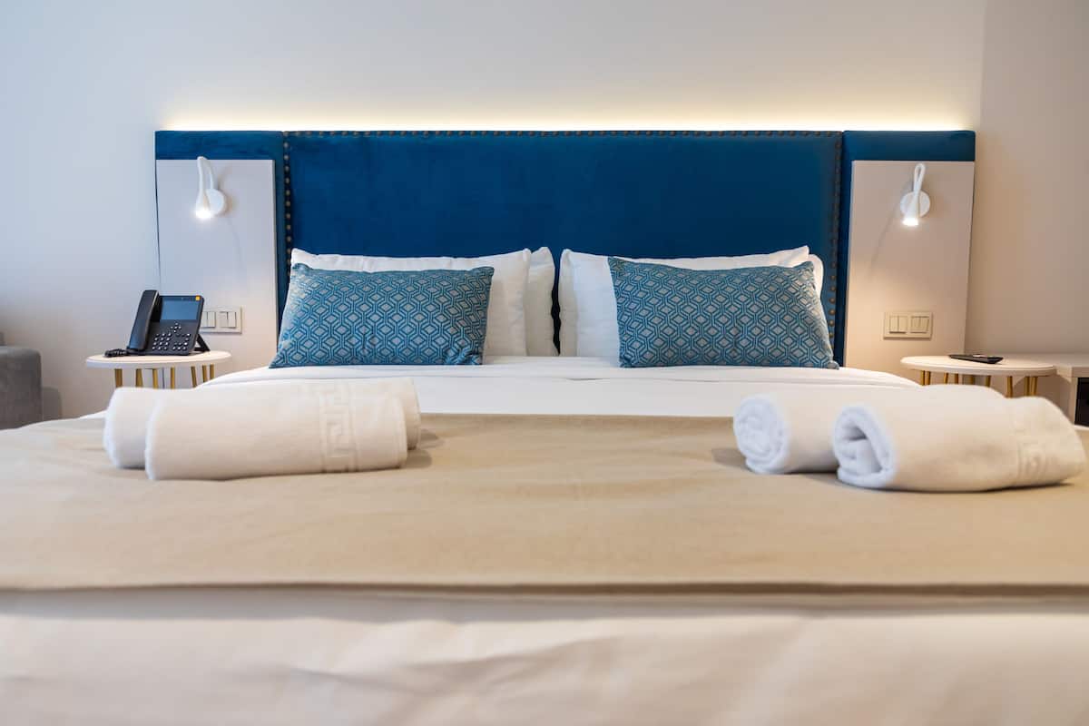 Una cama bien hecha con dos toallas enrolladas, un teléfono en la mesita de noche y almohadas estampadas.