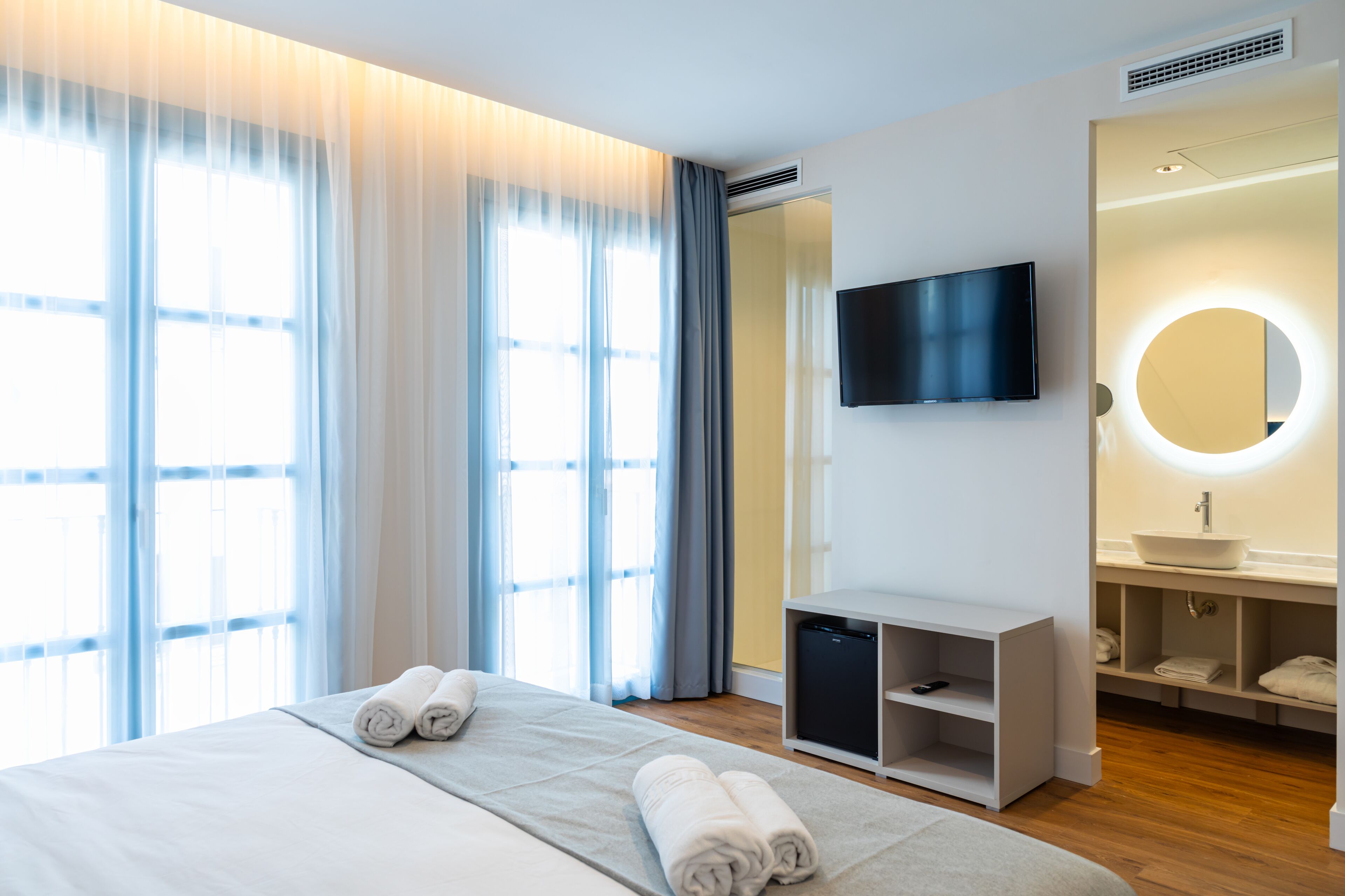 Moderni hotellihuone, jossa on suuri sänky, taulu-tv, peilillä varustettu meikkipöytä ja pieni työpöytä.