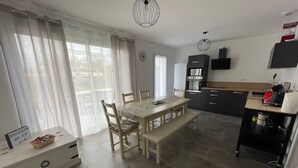Cocina moderna con comedor, que incluye una mesa grande, sillas y un banco. Hay una isla de cocina con un fregadero y un refrigerador.