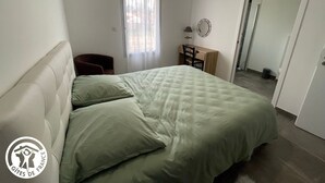 Un dormitorio con cama, escritorio, silla, ventana con cortinas y puerta que da a otra habitación.